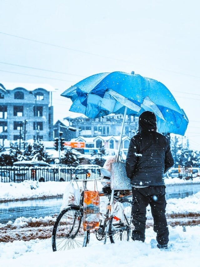 Person with umbrella and bicycle on snowy street during winter in Srinagar, Kashmir.