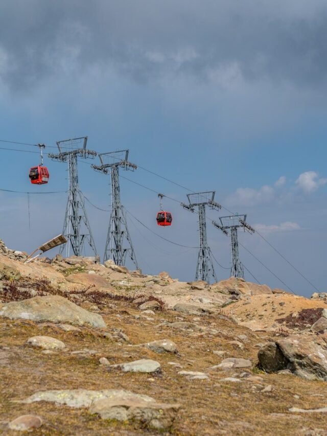 Red cable cars ascend mountain towers under cloudy sky